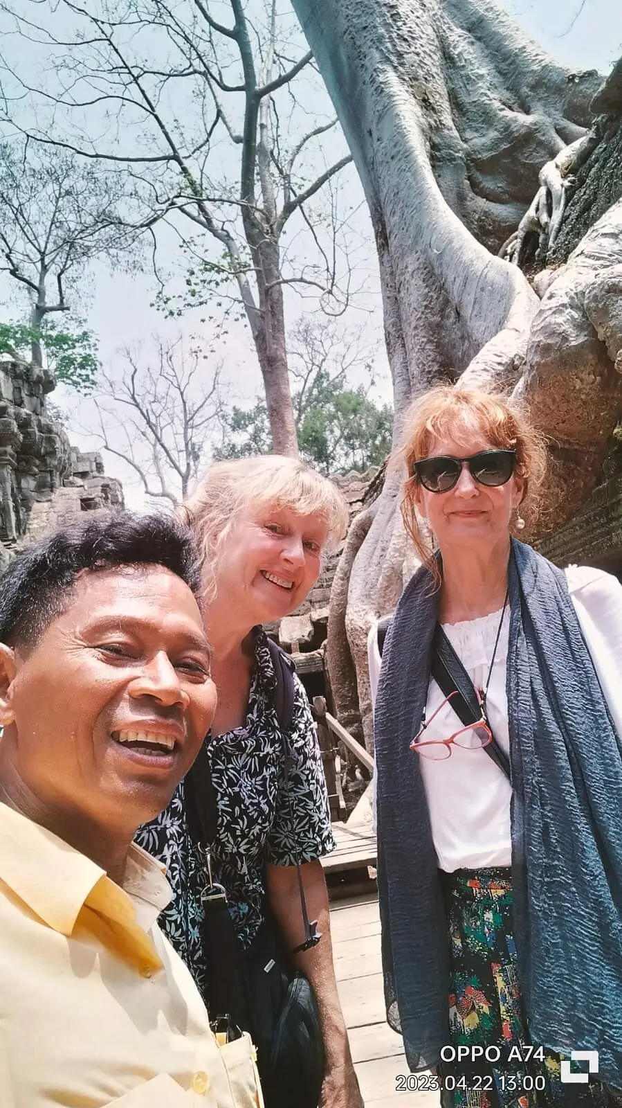San with two smiling travellers beside the giant tree roots of Ta Prohm